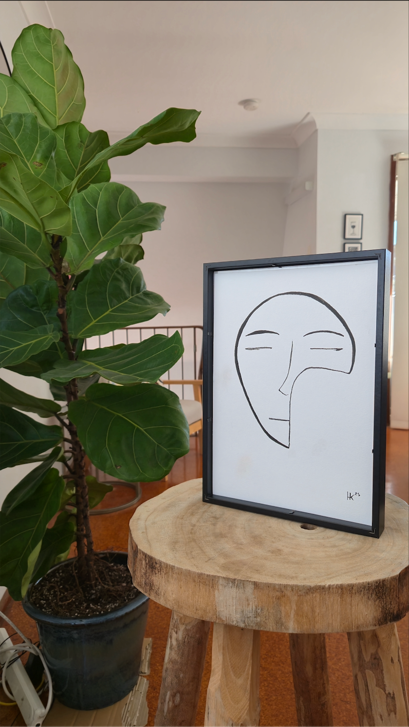 Framed abstract art on a wooden stool with a plant in the background